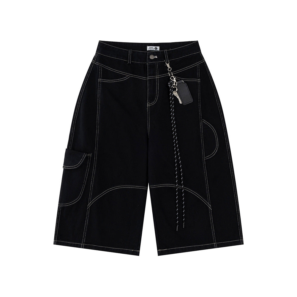 Front flat lay view of relaxed-fit long shorts in a deep dark black denim, featuring sharp contrast topstitching, asymmetrical utility paneling, a side cargo pocket, and a detachable lanyard with key ring and leather fob accents.