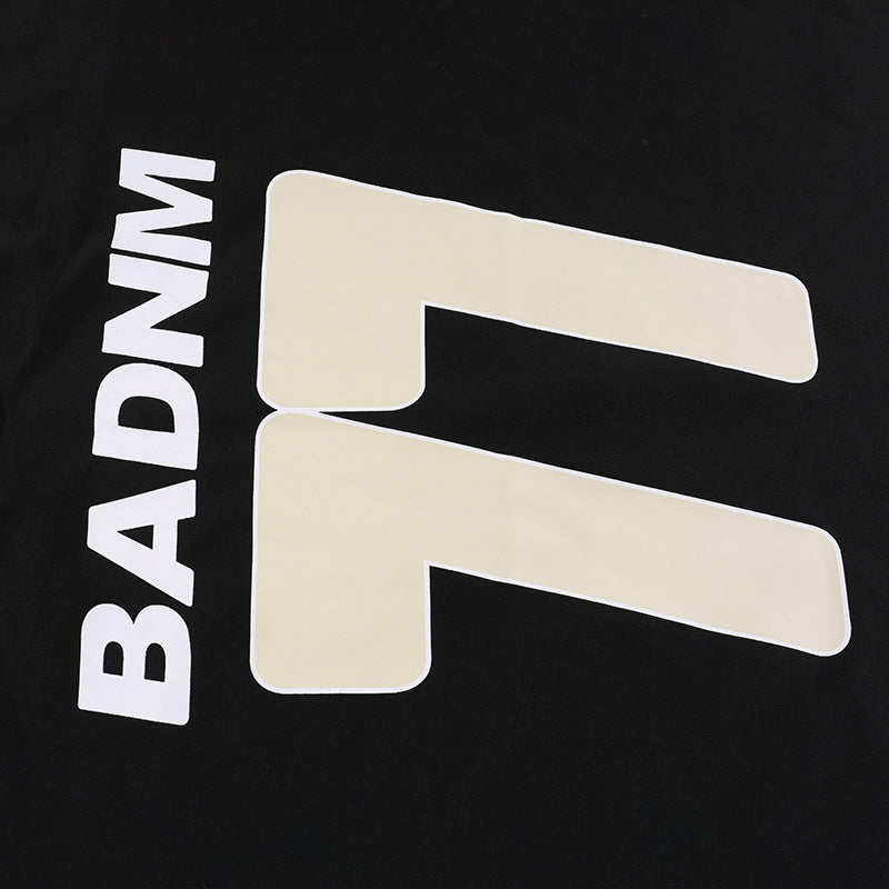 Close-up detail shot of the high-contrast cream white "BADNM 77" graphic print on the premium black fabric of the streetwear hoodie.