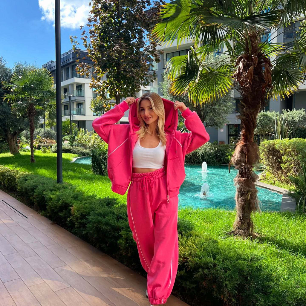 Front view of the premium two-piece tracksuit set in a vibrant fuchsia pink colorway, featuring a zip-front hooded sweatshirt and matching cinched-cuff sweatpants.