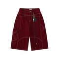 Front flat lay view of relaxed-fit long shorts in a deep burgundy denim, featuring sharp contrast topstitching, asymmetrical utility paneling, a side cargo pocket, and a detachable lanyard with key ring and leather fob accents.