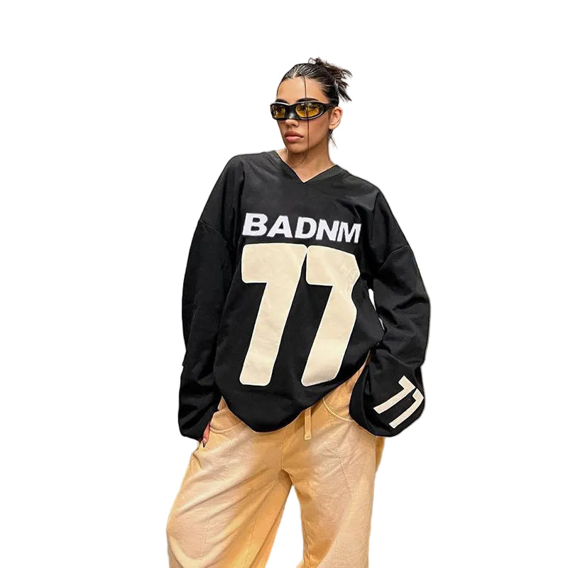 Streetwear style photo of a model wearing the oversized black "BADNM" jersey hoodie paired with wide-leg cargo pants in a warehouse setting.