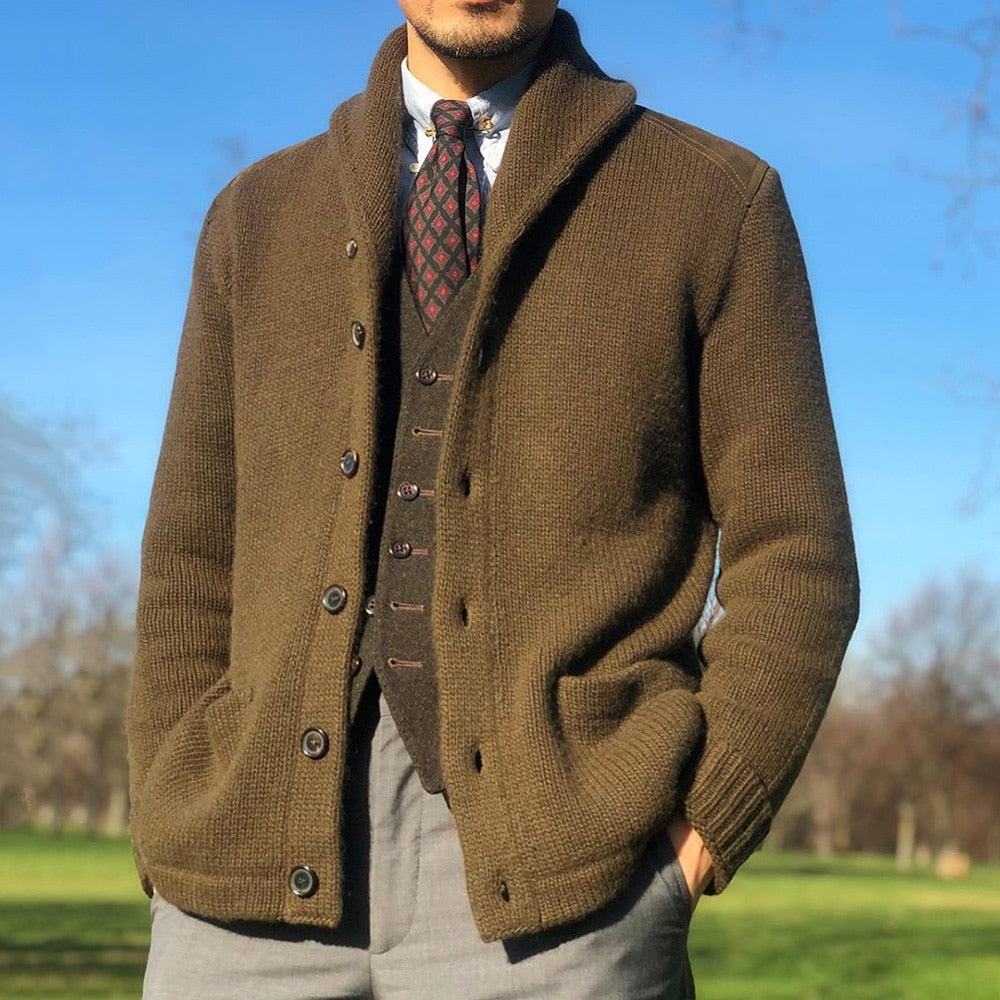 Man wearing the MontQuant Engineered Knit Button Jacket in Khaki, styled over a patterned tie, textured waistcoat, and grey trousers against a blue sky.