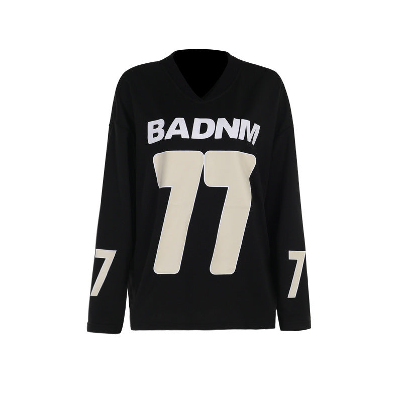 Front studio shot of a black oversized women's V-neck football jersey hoodie featuring a bold cream-colored "BADNM 77" graphic printed on the chest and numbers on the sleeves.